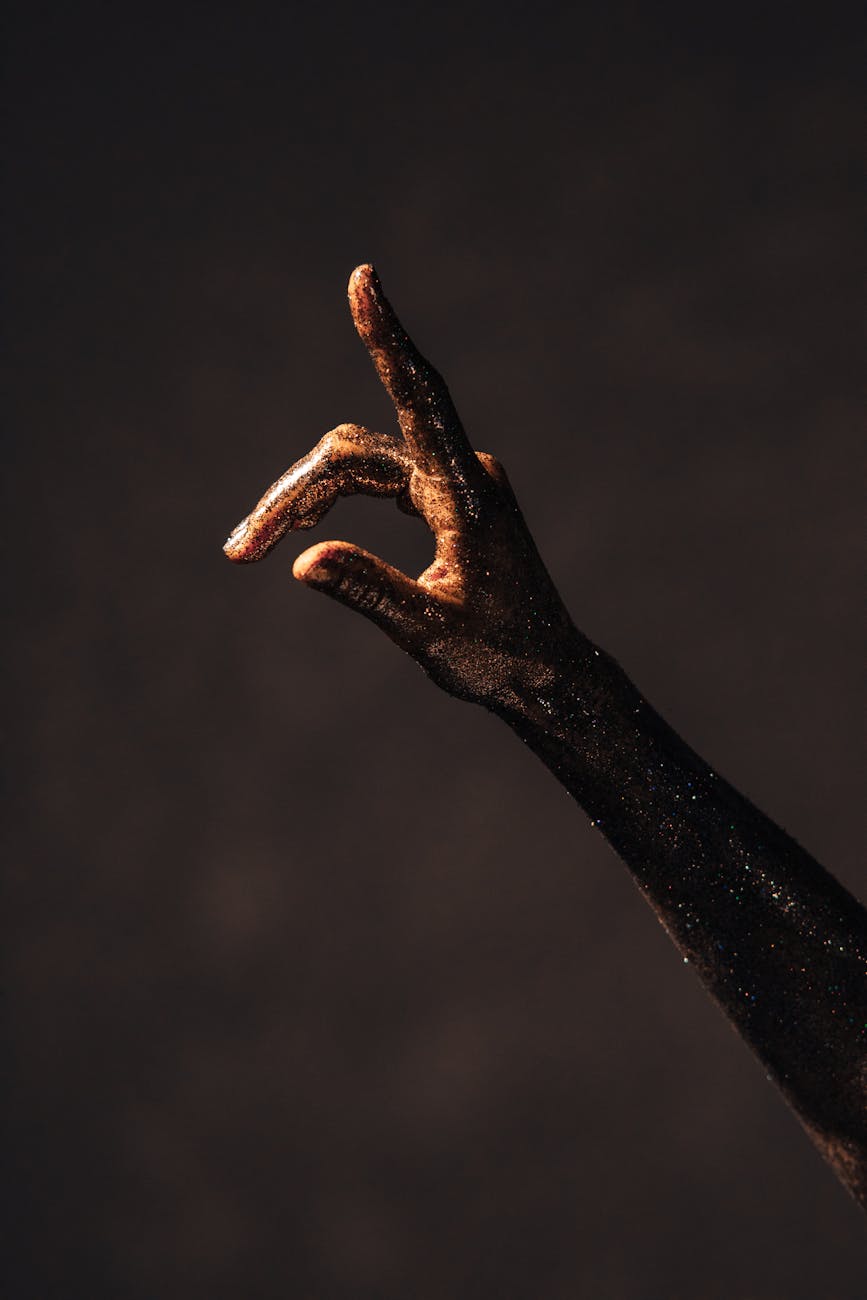 Image of a hand covered in gold glitter pointing upward with its index finger
